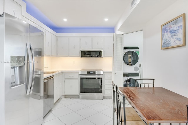 kitchen featuring white cabinetry, tasteful backsplash, light tile patterned floors, stainless steel appliances, and stacked washer / dryer