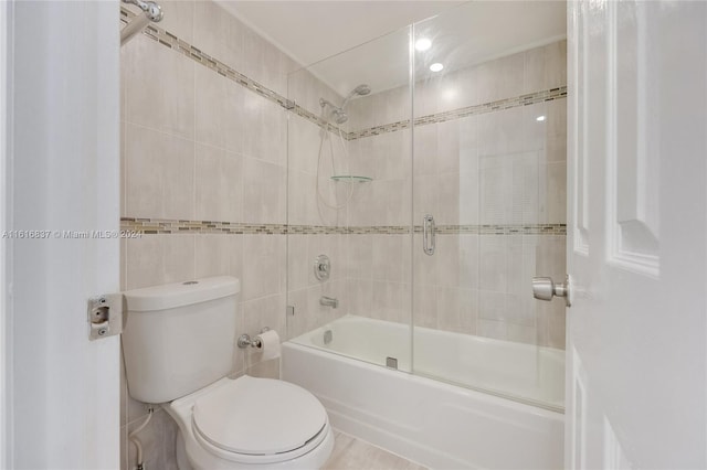 bathroom with tile walls, toilet, and combined bath / shower with glass door