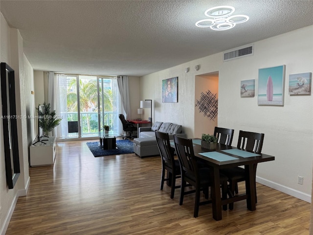 dining space with expansive windows, visible vents, a textured ceiling, and wood finished floors