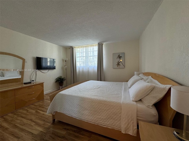 bedroom featuring a textured ceiling, wood finished floors, and a textured wall