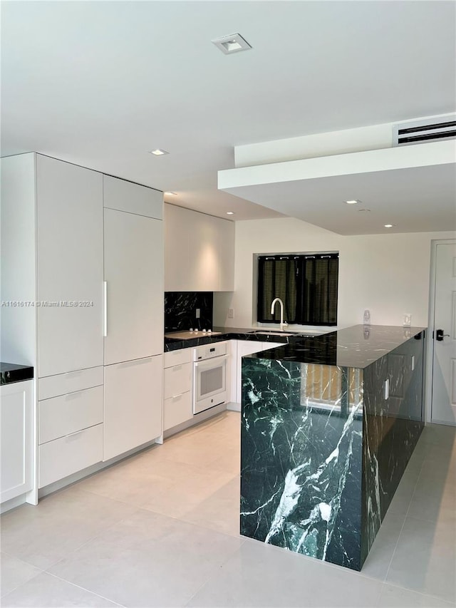 kitchen featuring oven, white cabinetry, light tile patterned floors, and dark stone counters