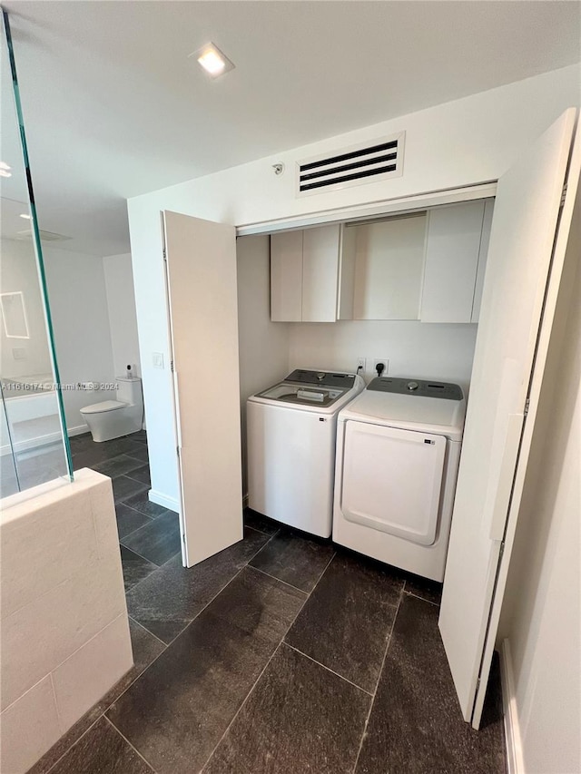 laundry area featuring dark tile patterned floors, washing machine and clothes dryer, and cabinets