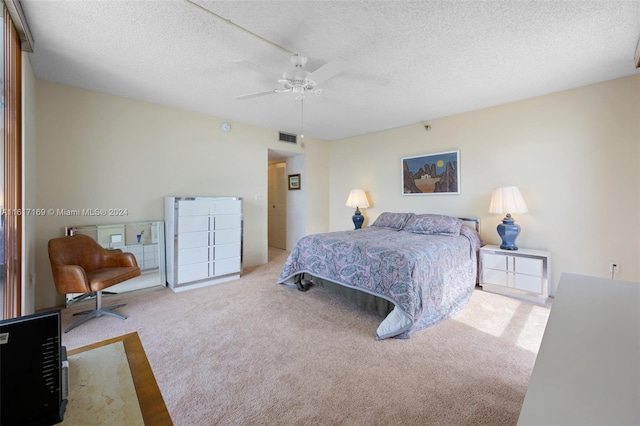 bedroom with ceiling fan, light colored carpet, and a textured ceiling