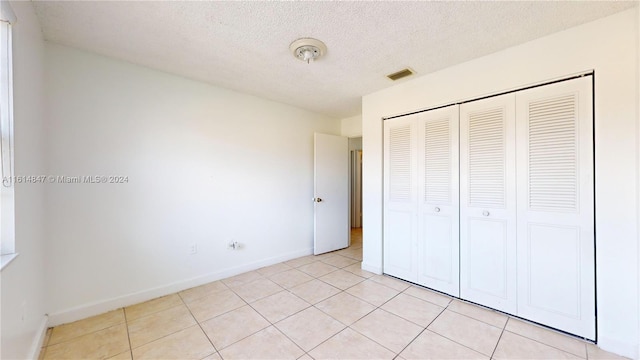 unfurnished bedroom featuring a textured ceiling, a closet, and light tile patterned floors