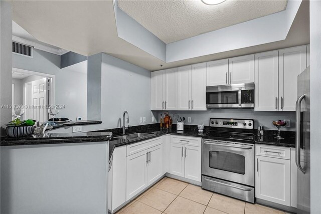 kitchen with white cabinetry, light tile patterned floors, dark stone counters, appliances with stainless steel finishes, and sink