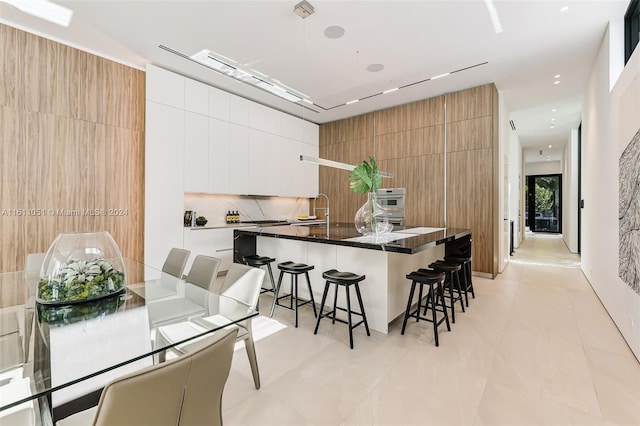 kitchen with sink, a breakfast bar area, white cabinets, decorative backsplash, and a center island with sink