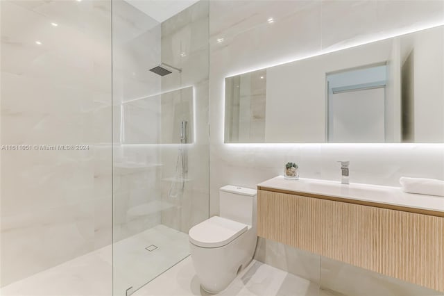 bathroom with tile walls, tiled shower, vanity, and toilet