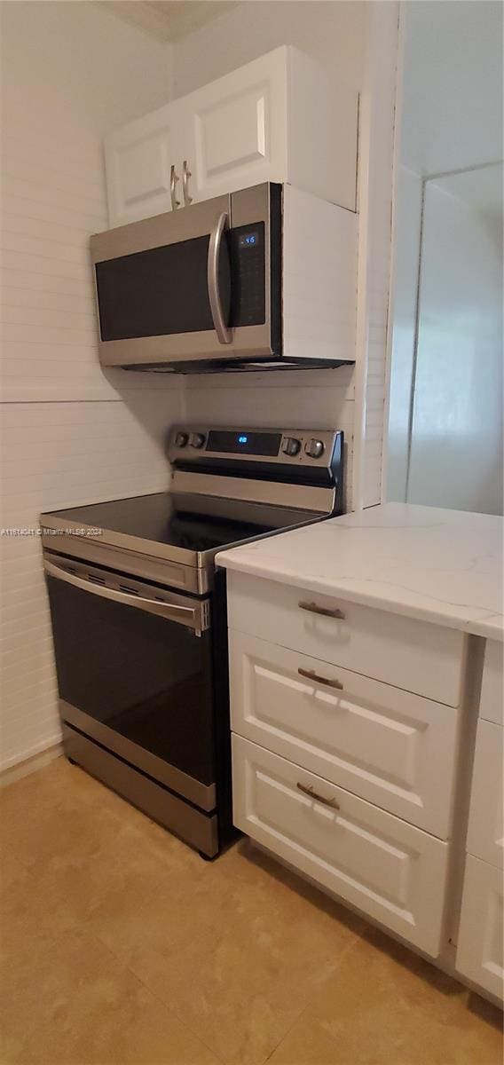 kitchen featuring appliances with stainless steel finishes, light tile patterned floors, white cabinets, and light stone counters