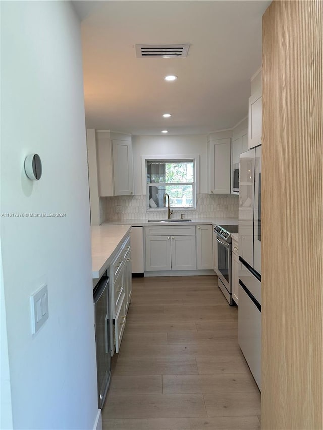 kitchen with light wood-type flooring, appliances with stainless steel finishes, backsplash, and white cabinetry