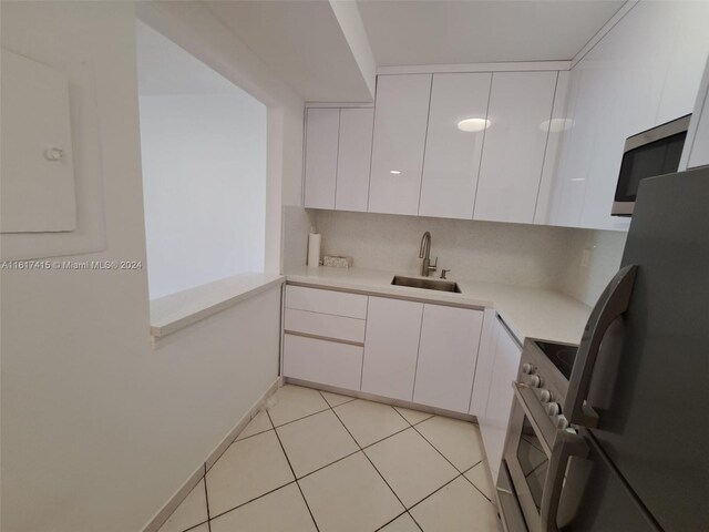 kitchen featuring light tile patterned flooring, white cabinetry, tasteful backsplash, appliances with stainless steel finishes, and sink