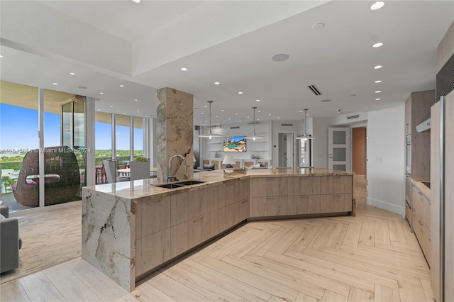 kitchen with a large island, light stone counters, sink, hanging light fixtures, and light parquet floors