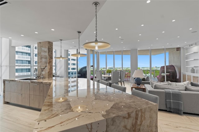 interior space with light stone counters, expansive windows, light brown cabinetry, decorative light fixtures, and sink