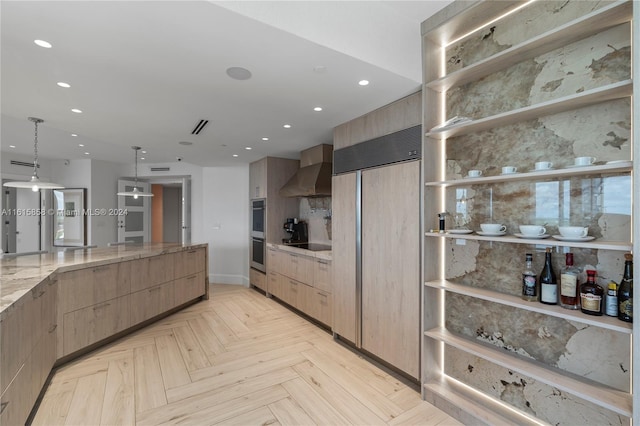 kitchen with light stone counters, decorative light fixtures, wall chimney exhaust hood, light parquet floors, and decorative backsplash