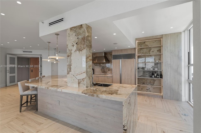 kitchen with wall chimney exhaust hood, a kitchen breakfast bar, light parquet flooring, and light stone countertops