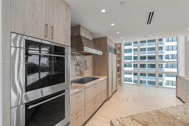 kitchen featuring light brown cabinets, wall chimney range hood, and light stone counters