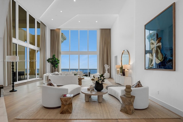 living room with a high ceiling, a water view, expansive windows, and hardwood / wood-style flooring