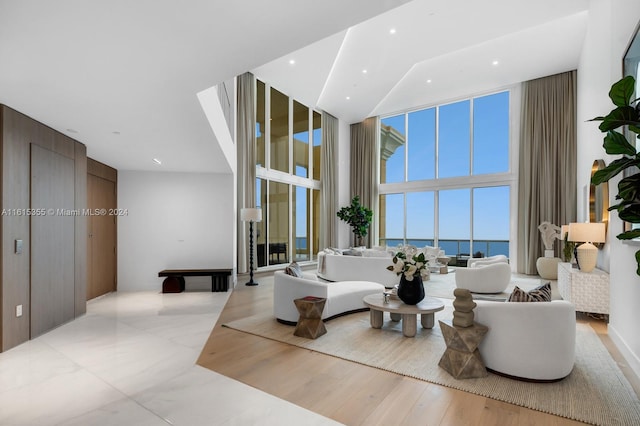 living room featuring a wall of windows, a water view, light wood-type flooring, and a high ceiling