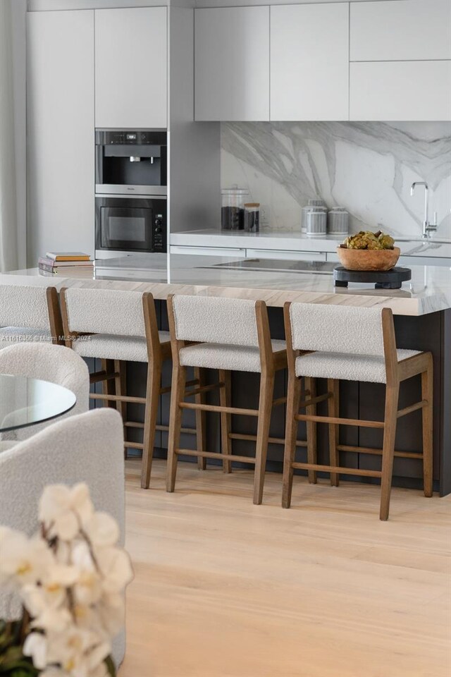 kitchen with a kitchen bar, white cabinetry, light wood-type flooring, and double oven