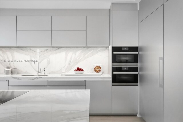 kitchen with sink, light stone counters, backsplash, and double oven