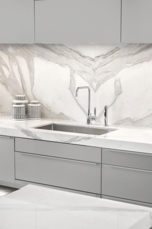 interior details with sink, light stone counters, and gray cabinetry