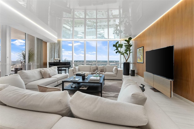 living room featuring light wood-type flooring, a high ceiling, wooden walls, and floor to ceiling windows