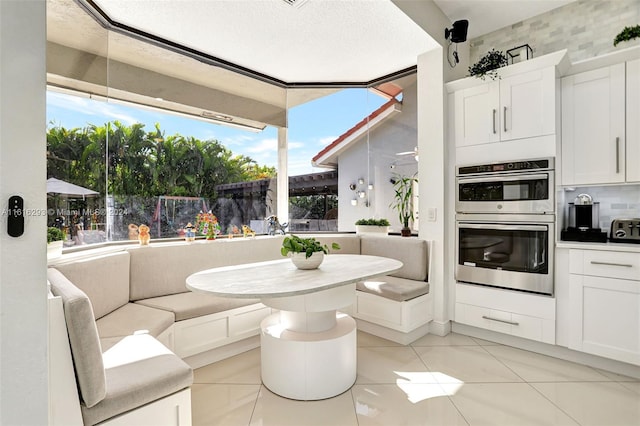 kitchen with a textured ceiling, light tile patterned floors, stainless steel double oven, tasteful backsplash, and white cabinetry