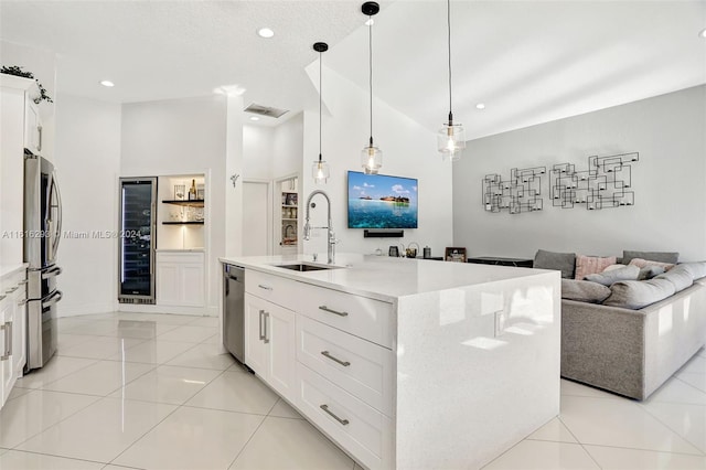 kitchen with white cabinets, a high ceiling, a center island with sink, decorative light fixtures, and sink