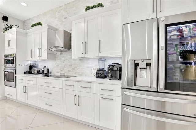 kitchen featuring tasteful backsplash, light tile patterned flooring, appliances with stainless steel finishes, white cabinets, and wall chimney exhaust hood