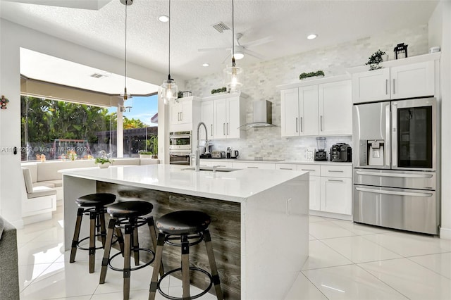 kitchen featuring wall chimney exhaust hood, stainless steel appliances, pendant lighting, and white cabinetry