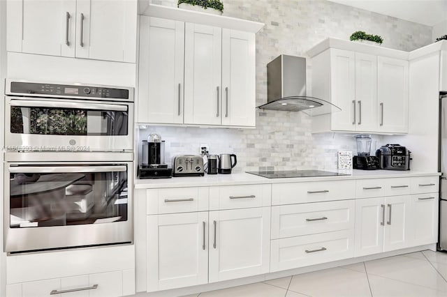 kitchen featuring double oven, light tile patterned flooring, white cabinetry, wall chimney range hood, and black electric stovetop