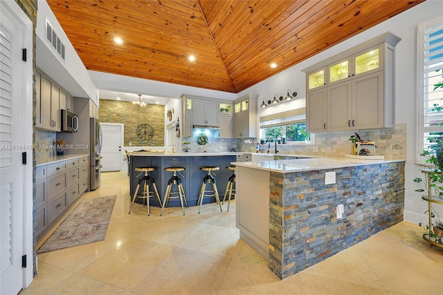 kitchen featuring a breakfast bar, gray cabinets, wooden ceiling, and appliances with stainless steel finishes