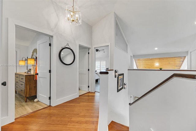 corridor featuring vaulted ceiling, light hardwood / wood-style flooring, and a notable chandelier