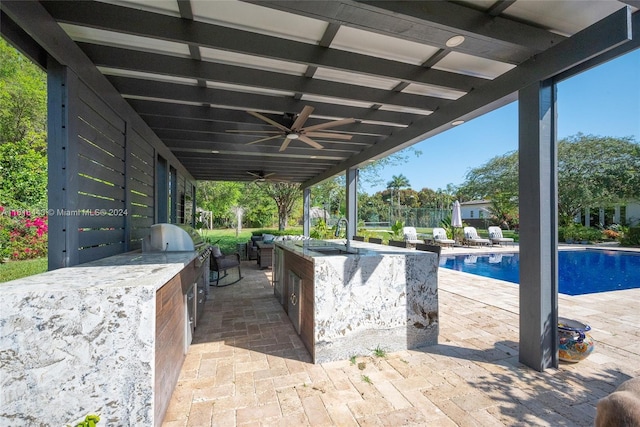 view of patio with an outdoor kitchen, ceiling fan, an outdoor wet bar, grilling area, and a fenced in pool