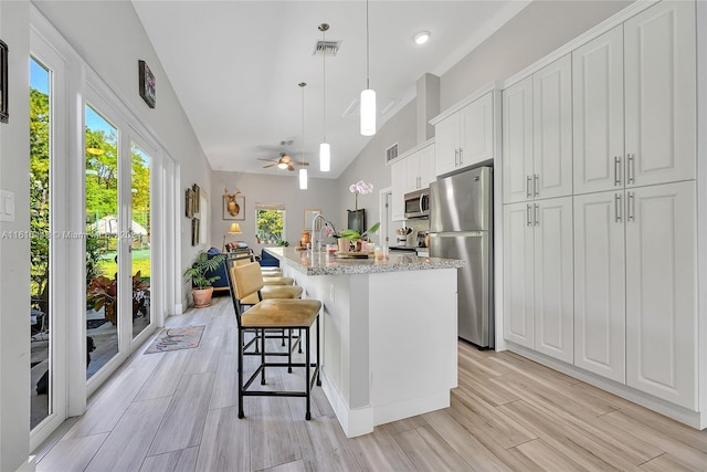 kitchen with ceiling fan, stainless steel appliances, decorative light fixtures, a center island with sink, and white cabinets