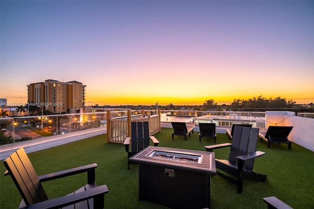 patio terrace at dusk with a fire pit, a balcony, and a yard