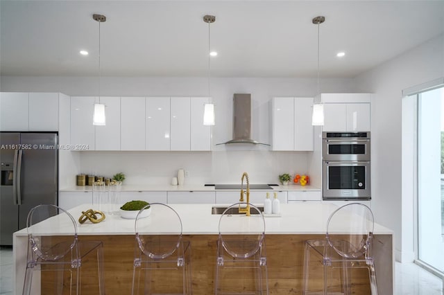 kitchen with decorative light fixtures, appliances with stainless steel finishes, wall chimney exhaust hood, and a center island with sink