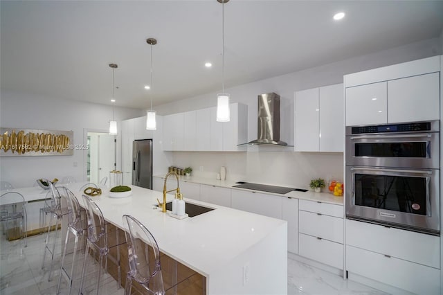 kitchen featuring wall chimney range hood, white cabinets, a kitchen island with sink, appliances with stainless steel finishes, and sink