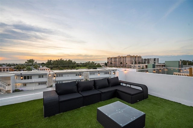 patio terrace at dusk featuring a balcony, a lawn, and an outdoor hangout area