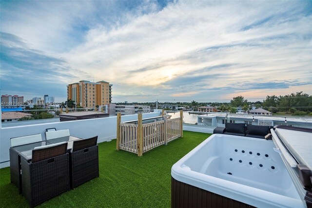 patio terrace at dusk featuring a lawn and a hot tub