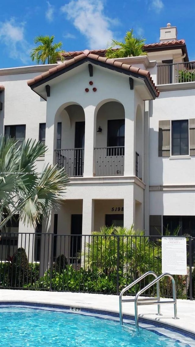 rear view of house featuring a tile roof, fence, and stucco siding