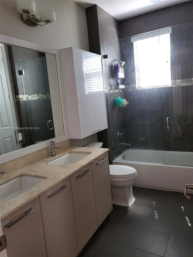 full bathroom with double vanity, bath / shower combo with glass door, tile patterned floors, and toilet