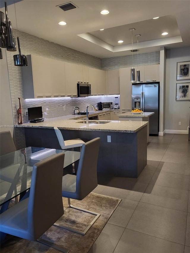 kitchen with a raised ceiling, visible vents, appliances with stainless steel finishes, a sink, and a peninsula