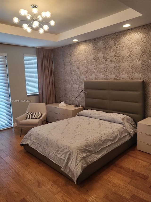 bedroom featuring a notable chandelier, wood finished floors, a raised ceiling, and wallpapered walls