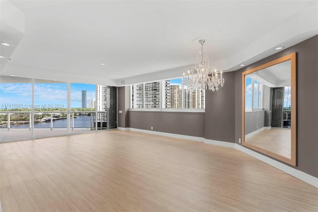 unfurnished living room with an inviting chandelier, a water view, and light hardwood / wood-style flooring