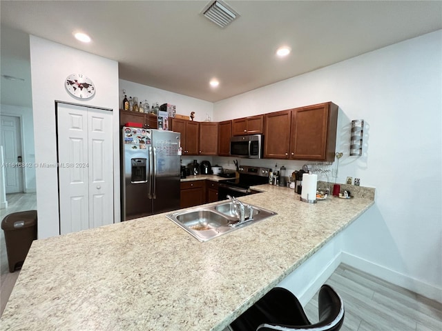 kitchen with kitchen peninsula, appliances with stainless steel finishes, light wood-type flooring, sink, and a breakfast bar area