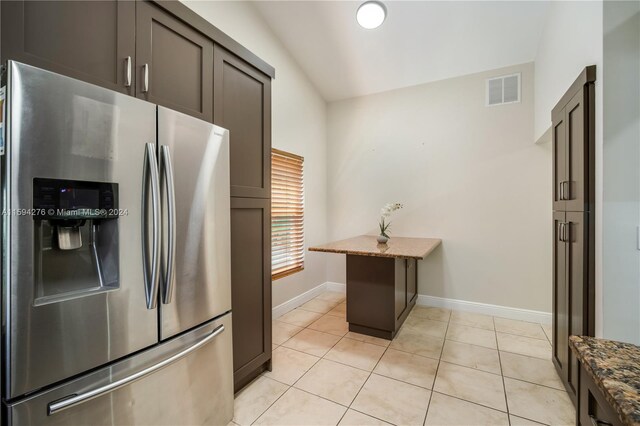 kitchen featuring stainless steel fridge with ice dispenser, light tile patterned floors, vaulted ceiling, and stone countertops