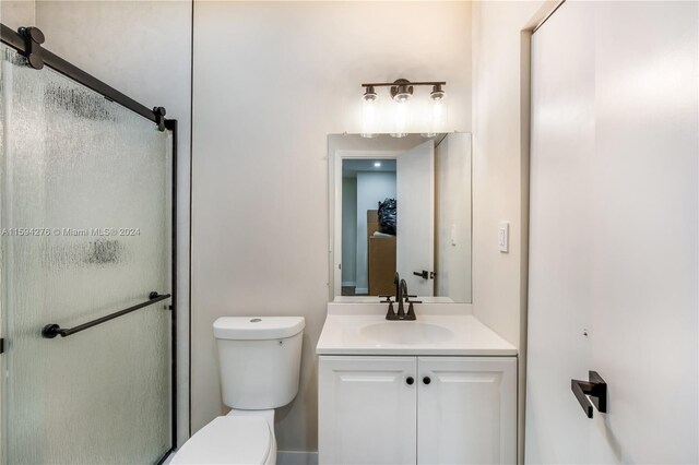 bathroom featuring a shower with door, vanity, and toilet