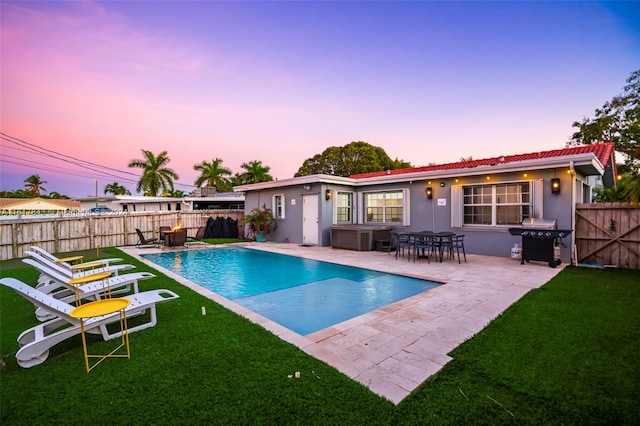 pool at dusk featuring a patio, grilling area, and a yard