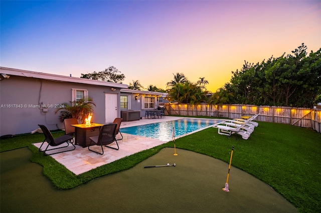 pool at dusk featuring a fire pit, a patio, and a lawn