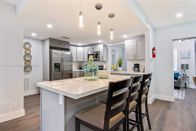 kitchen featuring dark hardwood / wood-style floors, appliances with stainless steel finishes, decorative light fixtures, a kitchen bar, and gray cabinetry